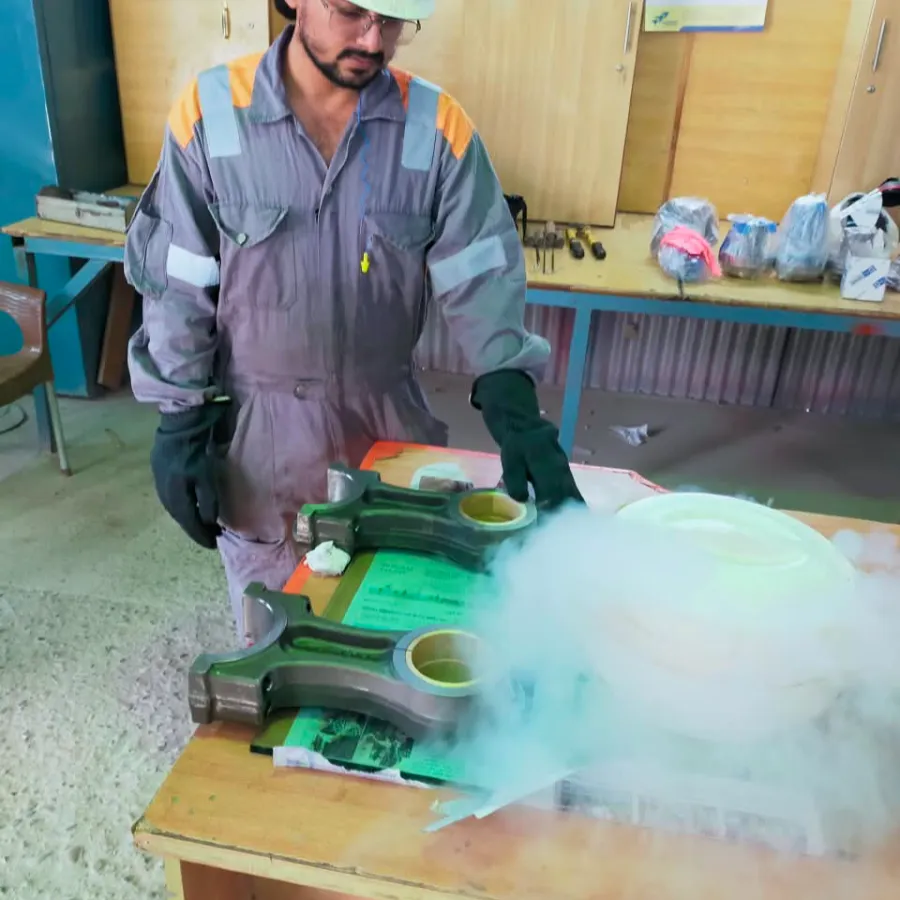 Technician shrink fitting connecting rod bushings with liquid nitrogen in the workshop